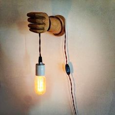 a light bulb that is attached to a wooden hand holding a string and plugged into the wall