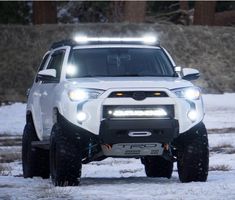 a white truck driving down a snow covered road with headlights on it's headlamps