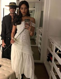 a woman in a white dress taking a selfie with a man standing next to her