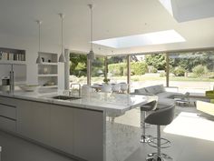 a modern kitchen with an island, bar stools and large windows looking out onto the backyard