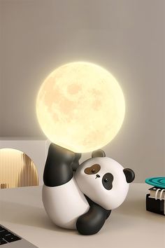 a panda bear sitting on top of a desk next to a laptop computer and lamp