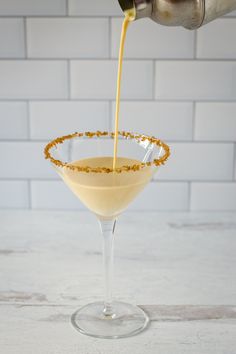 someone pouring orange juice into a martini in a coupe glass on a white countertop