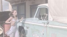 a woman standing next to an old blue truck