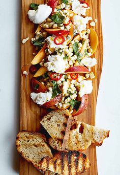 a wooden platter filled with grilled cheese, tomatoes and other foods on top of it