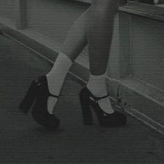 black and white photograph of woman in high heels leaning on railing with legs crossed, looking down