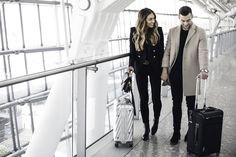 a man and woman holding hands while walking down a walkway with suitcases in hand