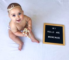 a baby is sitting next to a sign that says my rolls are homemade and holds a toy