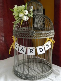 a birdcage that has some cards on it and flowers in the top one