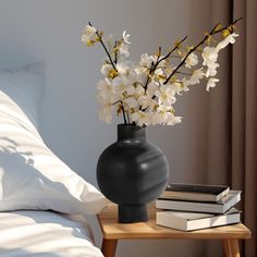 a black vase filled with white flowers on top of a table next to a bed