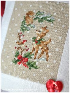 a close up of a cross stitch on a piece of cloth with a red heart