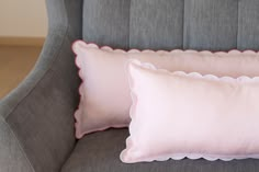 two pink pillows sitting on top of a gray couch