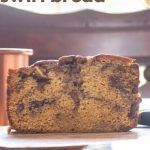 a loaf of cake sitting on top of a wooden table next to a coffee cup