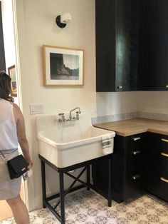 a woman is standing in front of a sink and counter top with black cabinetry