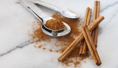 cinnamon sticks and powder in spoons on a marble counter top with utensils