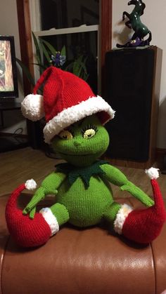 a green stuffed animal sitting on top of a brown leather couch wearing a santa hat