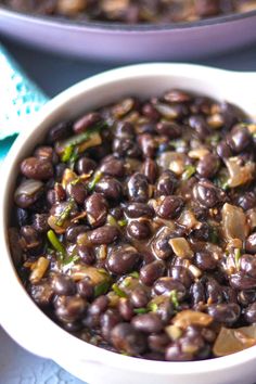 a bowl filled with beans and onions on top of a blue table cloth next to another bowl