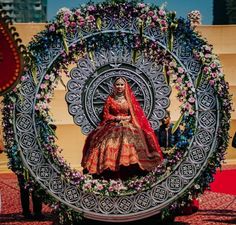 a woman in a red and gold wedding dress is sitting on a large metal object