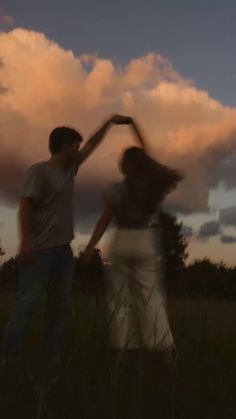 two people standing in the grass with their arms around each other and one person reaching for something