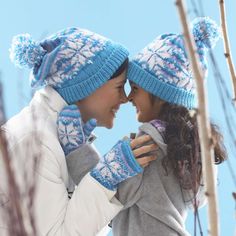 two young women wearing knitted hats and mittens, one is kissing the other