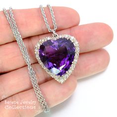 Purple Amethyst has a special place in our hearts, there is no other gemstone with a rich deep purple as pure Amethyst! This pendant necklace sports a heart shaped Purple Amethyst surrounded by a halo of white sparkly diamonds! An 18k white gold chain completes the piece. Total Weight: 19.23 grams Size: 1.5 inches tall (including bail), 1.1 inches wide Precious Metal: 18k white gold Precious stones: -Amethyst Center Stone: 23mm x 23mm, 33 carats -White Round Diamonds: 1.38 carats, 2.5mm Hallmark Purple Heart Pendant Necklace For Formal Occasions, Formal Purple Heart Pendant Necklace, Formal Heart Cut Amethyst Jewelry, Purple Heart Cut Jewelry For Formal Occasions, Luxury Purple Necklace For Anniversary, Purple Heart Cut Jewelry For Formal Events, Luxury Purple Necklaces For Anniversary, Formal Purple Necklace With Polished Finish, Purple Diamond Necklace