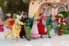 several people dressed in costumes dancing on a stage with christmas trees and decorations behind them