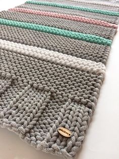 a close up of a knitted blanket on a white tablecloth with a wooden button