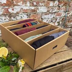 an open cardboard box filled with socks on top of a wooden table next to flowers