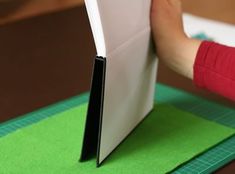 someone is cutting out an origami book on a green piece of paper with scissors