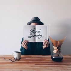 a person sitting at a table holding up a book with the words good morning written on it