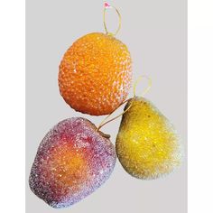 three pieces of fruit that are covered in colored powdered sugar and hanging from strings