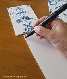 a person holding a pen and writing on some paper with blue drawings behind them,