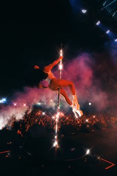 a woman is doing tricks on a pole in front of an audience at a concert