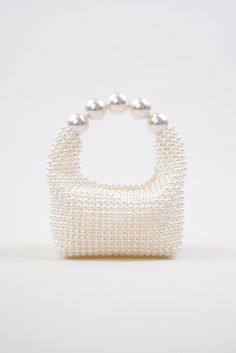 Introducing the stunning Nuit Blanche Pearl Bag by Vanina, a true embodiment of luxury and sophistication. Impossibly chic, this exquisite bag is a true masterpiece of artistry and craftsmanship that will become a wedding piece you will cherish for years to come. This bag boasts a radiant, iridescent white hue that shimmers and sparkles in the light, adding an ethereal and enchanting touch to your ensemble. Each pearl has been meticulously hand-sewn onto the bag, creating a seamless, flawless finish that exudes elegance and refinement. All of Vanina's pieces are handcrafted by skilled artisans in Lebanon, using ethically sourced and sustainable materials, making it an environmentally conscious choice you can feel good about. White All-over faux pearl embellishments Curved beaded top handle High-end White Box Bag For Gifts, Luxury Box Bag With Top Carry Handle For Party, Luxury Square Clutch With Detachable Handle, Luxury Party Box Bag With Top Carry Handle, Designer White Rectangular Evening Bag, White Top Handle Box Bag For Party, Luxury Evening Bag With Round Handle For Party, Designer Formal Evening Bag With Handle Drop, High-end Top Handle Bags For Party