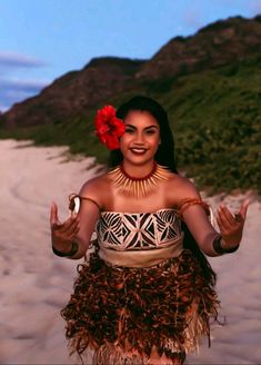 a woman wearing a hula skirt and holding a flower in her hand on the beach