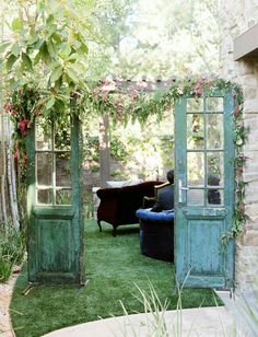 an old door is open on the grass in front of a couch and table with flowers