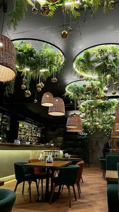 the interior of a restaurant with plants hanging from the ceiling and green chairs on the tables