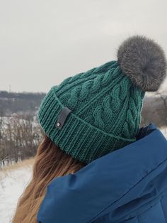 a woman wearing a green hat with a fur pom in the middle of it