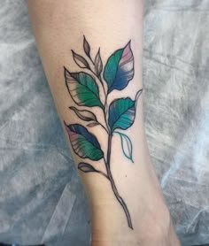 a tattoo on the foot of a person with a green and blue leaf in it