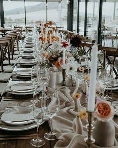 the table is set with white and orange flowers in vases, silverware, and candlesticks