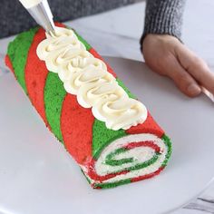 a person cutting into a cake with white frosting and green and red icing