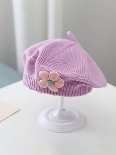 a purple hat with a flower on it sitting on top of a white table next to a window