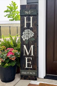 a wooden sign that says our home and has flowers in the pot next to it