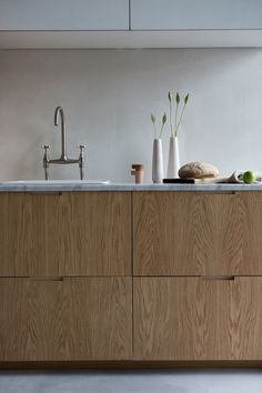 a kitchen with wooden cabinets and marble counter tops, white vases on the sink