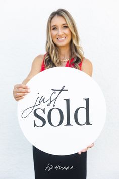 a woman holding up a sign that says just sold in black and white writing on it