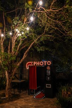 an outdoor stage set up with red curtains and lights on the trees in front of it