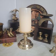 a white candle sitting on top of a table next to brass cups and candlesticks