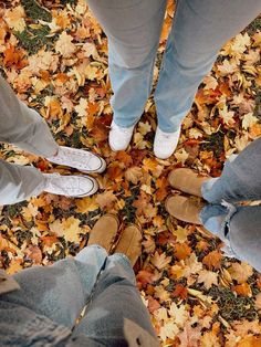 four people standing in a circle with leaves on the ground and one person wearing white shoes