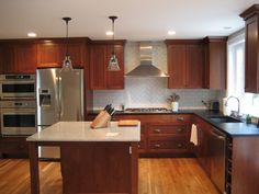 a large kitchen with wooden floors and stainless steel appliances in the center, along with dark wood cabinets