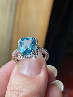 This lovely ring features a 3.56 carat Swiss Blue Topaz which is IF clarity. The Topaz boasts a Checkerboard Cut which aids in it's sparkle and beauty! It measures 10x8mm, and is surrounded by Natural White Topaz. The setting is Sterling Silver which has a Rhodium coating, keeping it from tarnishing.  This ring is a finger size 8. It will arrive in a nice little gift box and ready for a bow!  Thank you for looking! Luxury Blue Topaz Halo Ring, Blue Topaz Cushion Cut Ring With Halo Setting, Cushion Cut Blue Topaz Ring With Halo Setting, Aquamarine Ring With Halo Setting For Anniversary, Blue Topaz Cushion Cut Diamond Ring, Cushion Cut Blue Topaz Rings With Diamond Accents, Princess Cut Topaz Ring With Accent Stones, Cushion Cut Topaz Ring With Halo Setting, Fine Jewelry Cushion Cut Topaz Ring With Center Stone