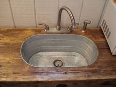 an old metal sink sitting on top of a wooden counter next to a white wall